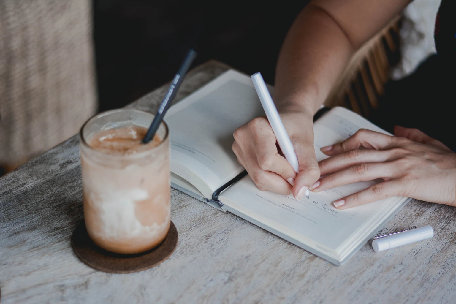 A person writing in a journal beside a cup of coffee