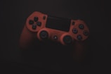 A red gaming controller with various buttons and joysticks is placed against a dark background, highlighting its features.