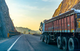 An HGV truck on a winding country road bordered by fields and hills at sunset.