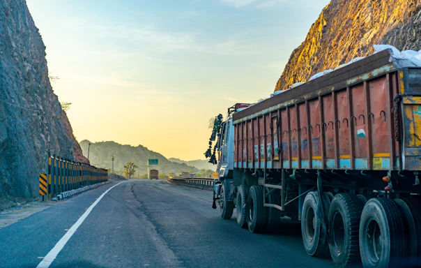 A mechanic assisting a mining truck on a rugged mountain road at sunset.