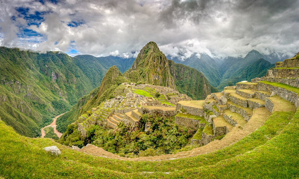 green grass field and green mountains under white clouds and blue sky during daytime