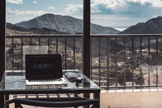 A friendly freelancer working on a laptop with Swiss mountains visible through the window.