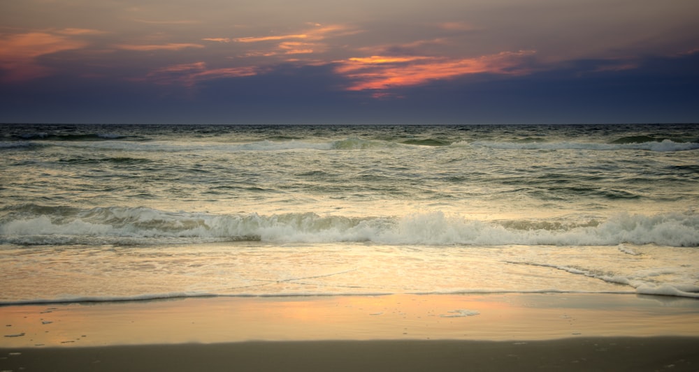 ocean waves crashing on shore during sunset