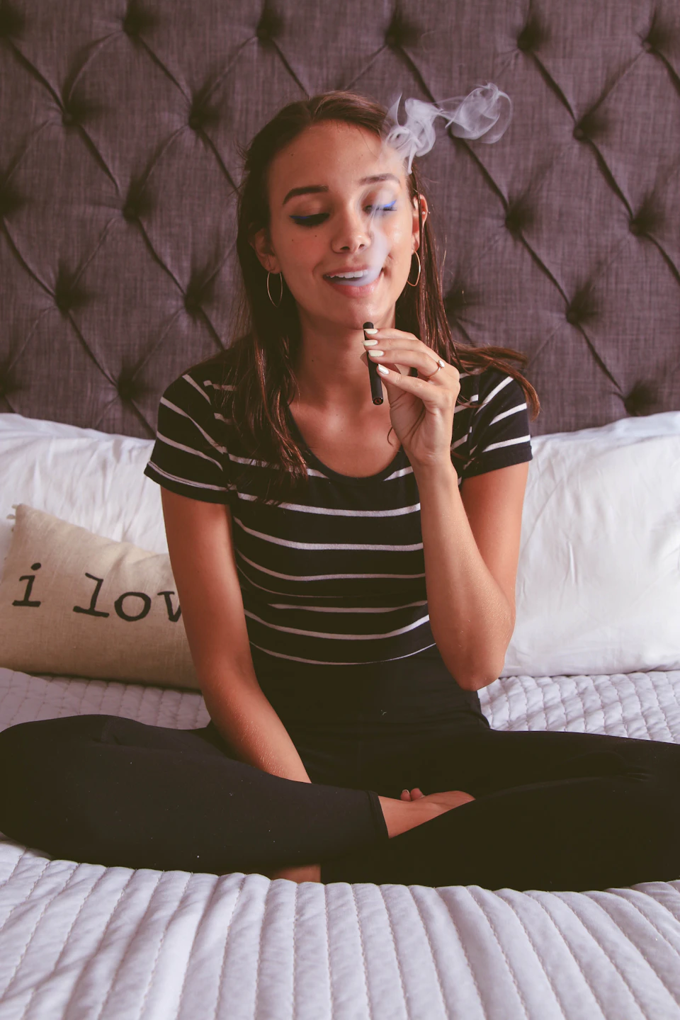 Young woman sits comfortably on a bed with white sheets and black striped shirt