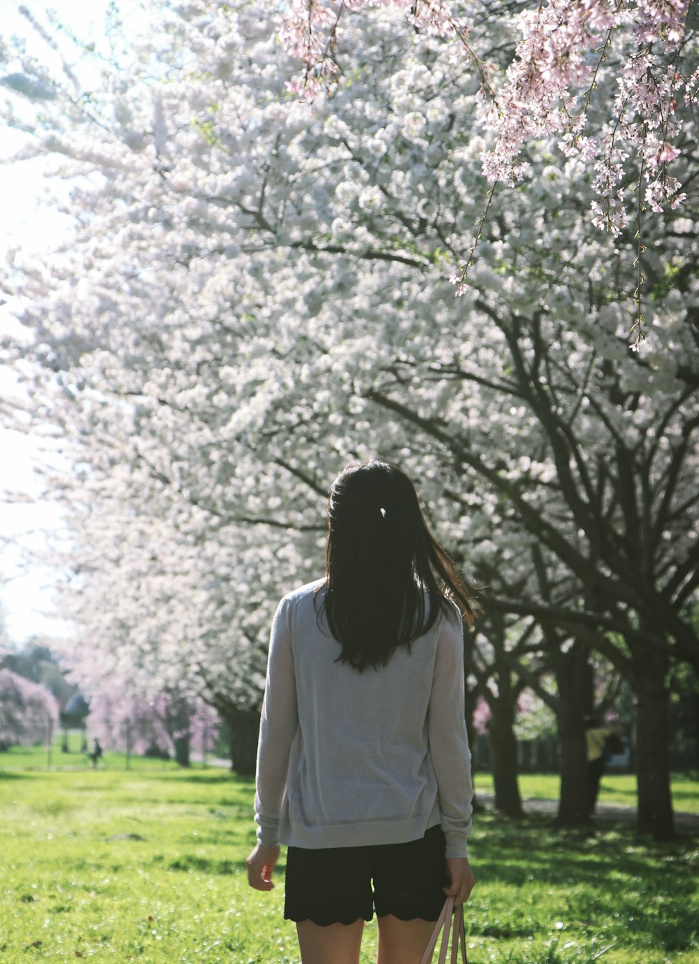 昼間、木々の近くの緑の芝生の上に立つ白い長袖シャツを着た女性