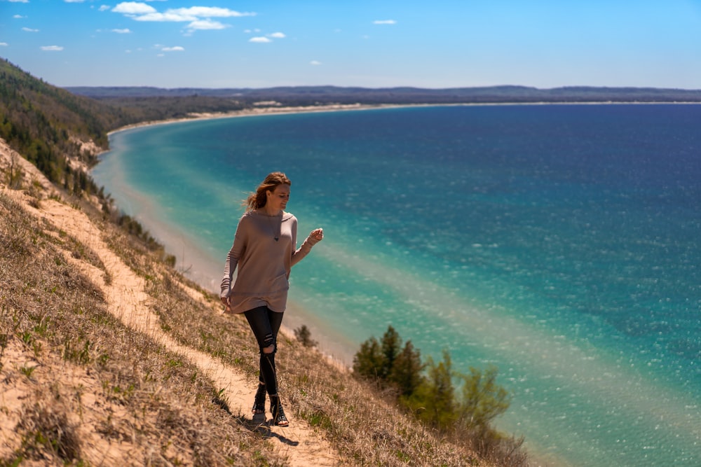 woman in white long sleeve shirt and black pants standing on brown field near body of near on on with