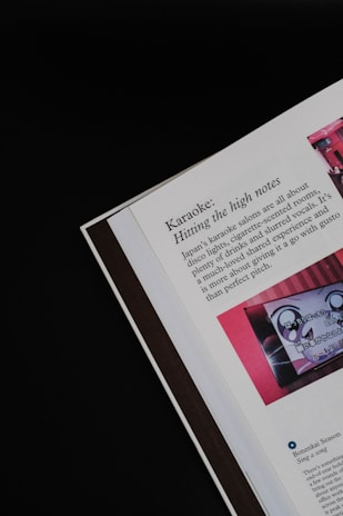 An open page of a book or magazine lies partially viewable against a black background. The prominent topic is 'Karaoke: Hitting the high notes,' which describes Japan's karaoke salons. There is an image with red tones next to the text, depicting what seems to be a karaoke machine or screen.