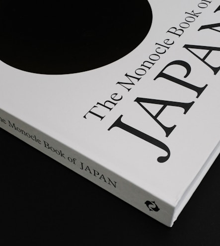 A close-up of a book titled 'The Monocle Book of Japan' with a sleek black and white cover. The book is positioned on a dark surface, creating a contrast with its white cover that features bold black text and a minimalist design.