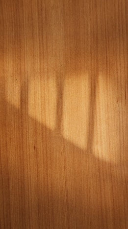 A warm brown wooden texture with sunlight casting soft shadows.