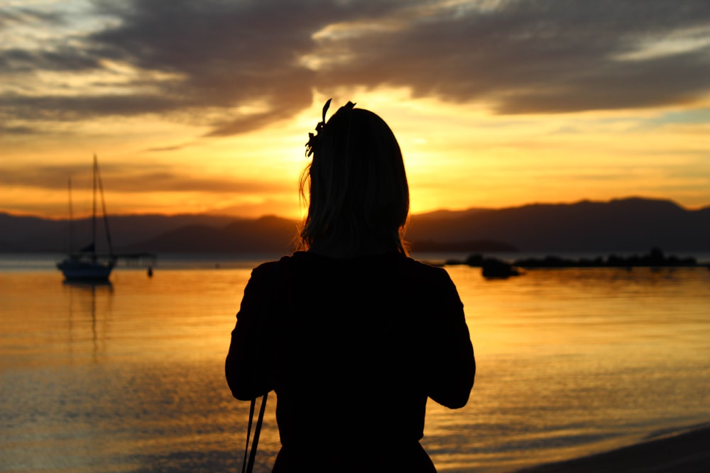 silhouette of woman standing on seashore during sunset