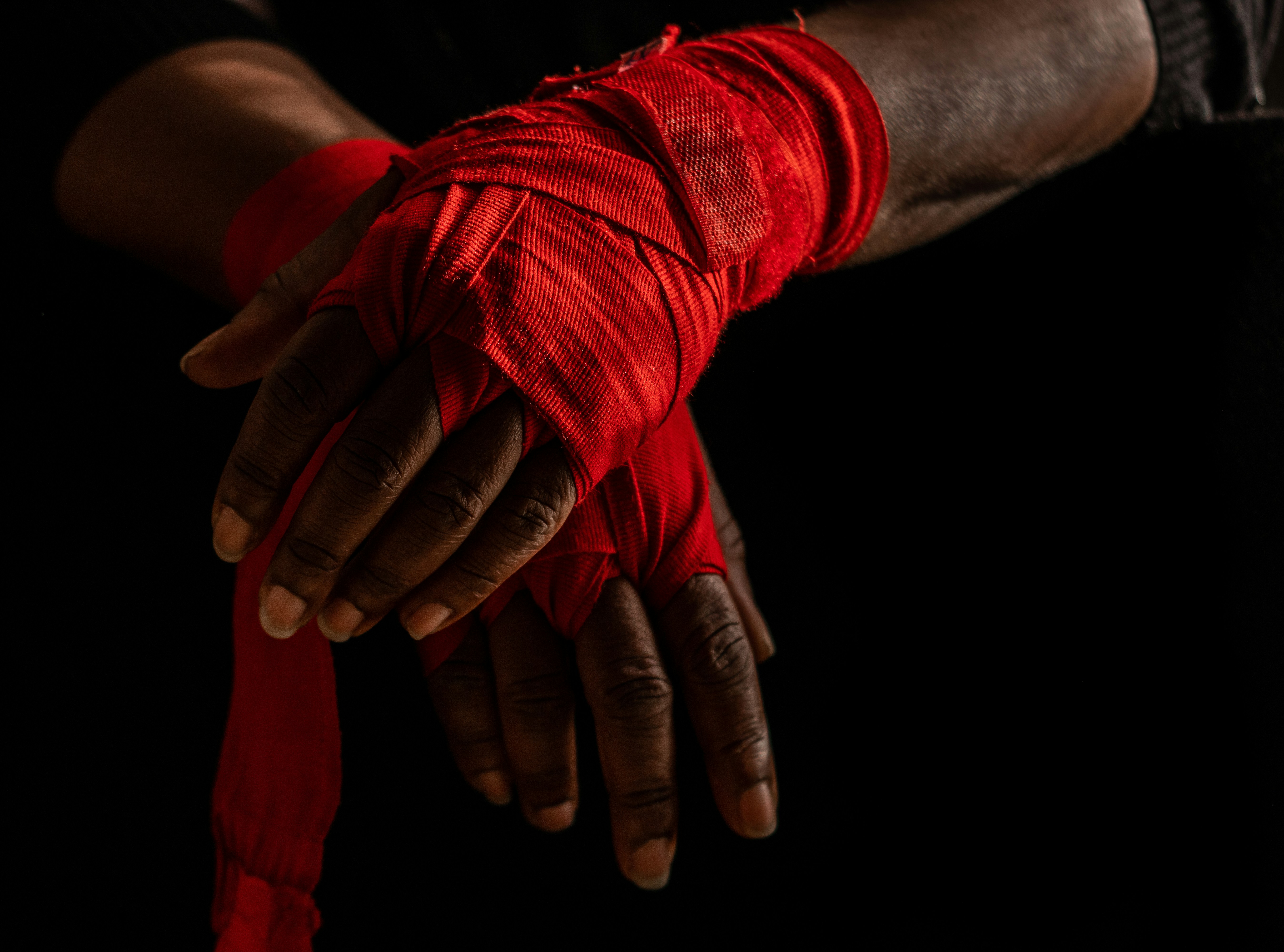 Hands with a dark skin tone, and some wrinkles, wrapped in red fabric like bandages.