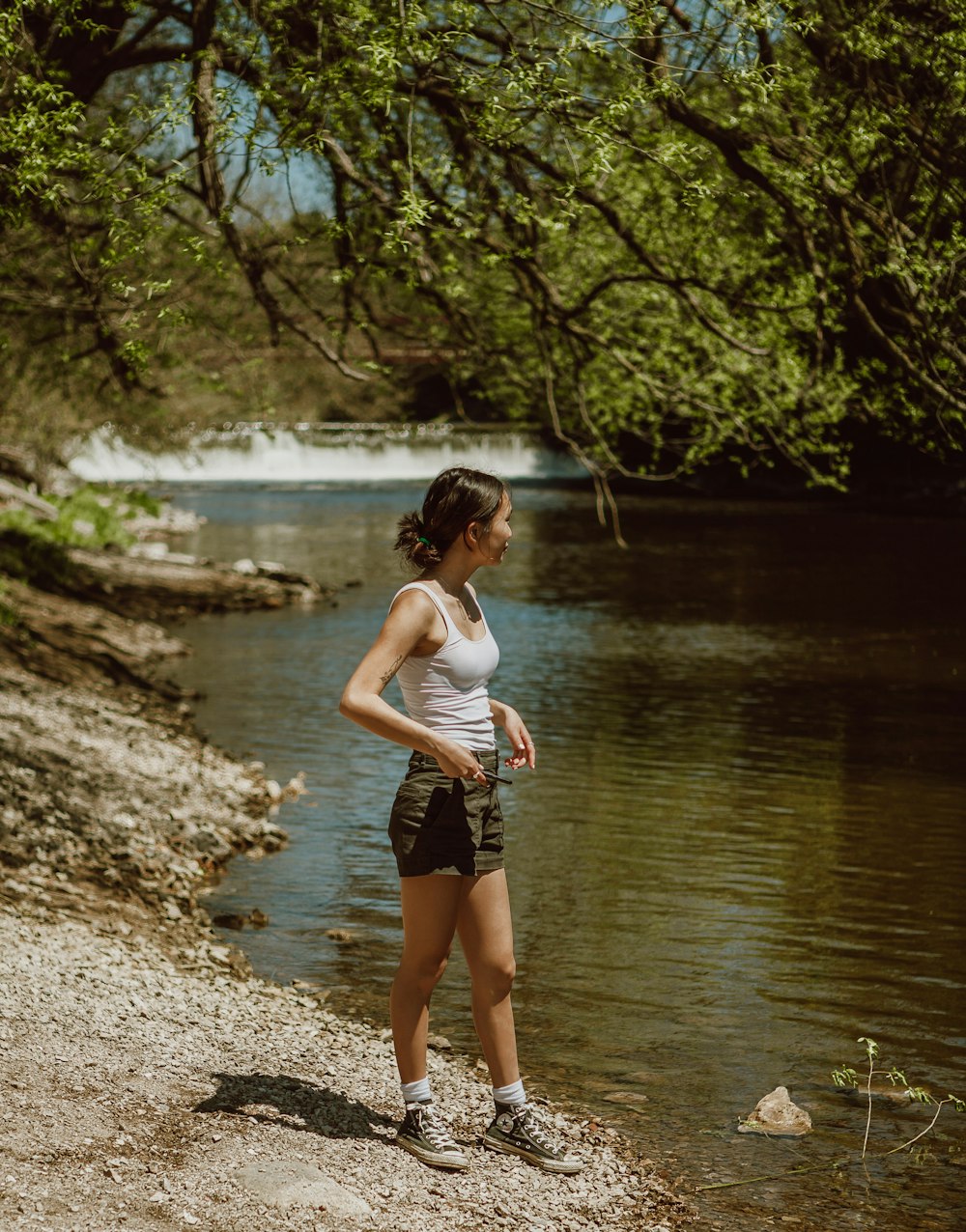 白いタンクトップと黒い短パンを着た女性が昼間、川に立っている
