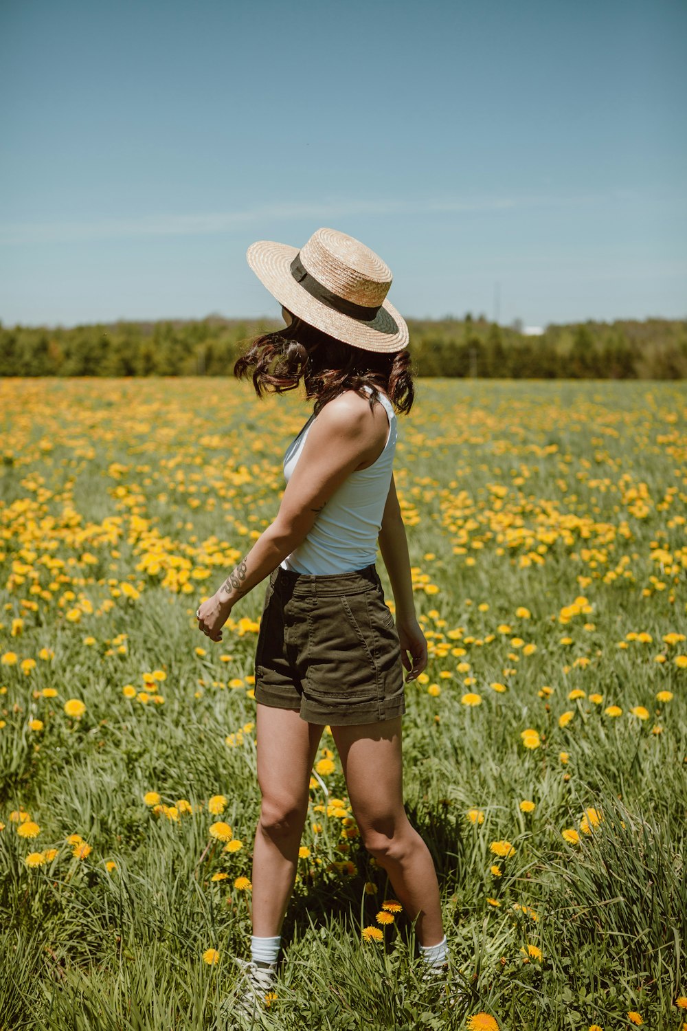 昼間、黄色い花畑に立つ白いタンクトップと黒いスカートの女性