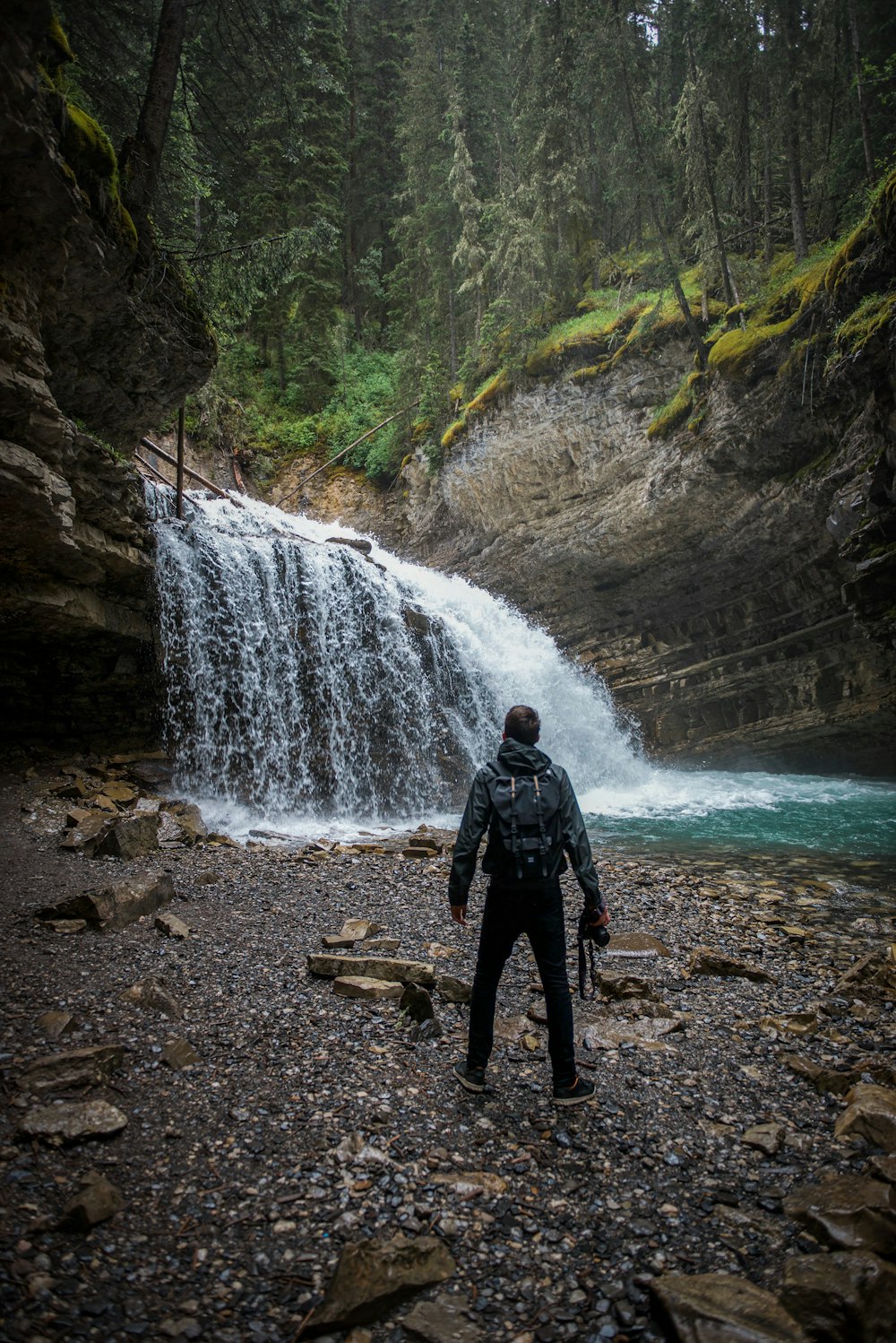 Mann in schwarzer Jacke tagsüber in der Nähe von Wasserfällen