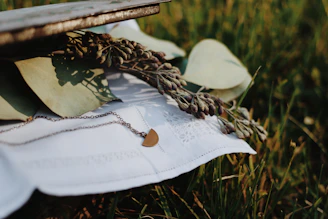 A delicate gold necklace resting softly on a cream linen background with a hint of dried flowers.