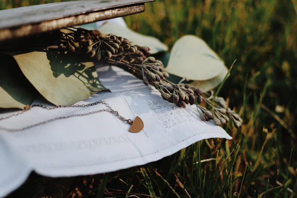 A delicate gold necklace resting softly on a cream linen background with a hint of dried flowers.