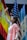 A young person dressed in a white and pink outfit is reaching upward in a pose. Behind them are national flags including those of Spain, the United States, and Guatemala, suggesting a multicultural or international event.