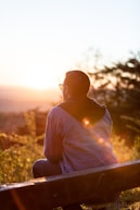 woman in white shirt and sunglasses sitting on brown wooden bench during sunset