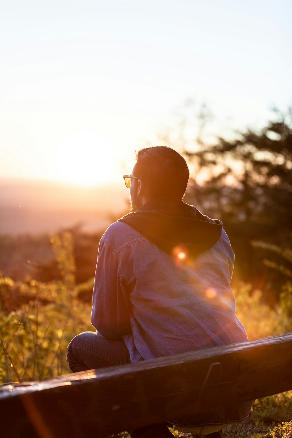 Frau in weißem Hemd und Sonnenbrille sitzt bei Sonnenuntergang auf brauner Holzbank