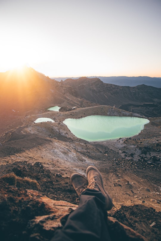 person in brown hiking shoes sitting on rock formation during daytime in Tongariro National Park New Zealand