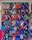 A collection of colorful luchador masks arranged on a grid display. Each mask features various designs, some with sports team logos and others inspired by superhero motifs. The masks are vibrant and include a range of colors and patterns.