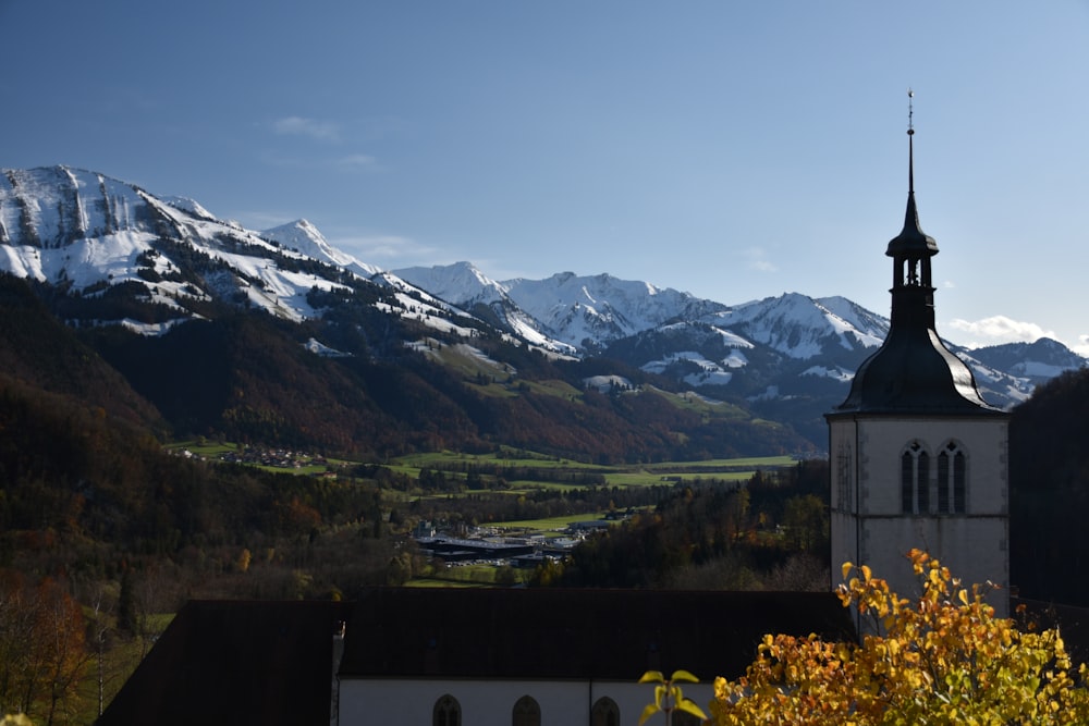 white and black concrete building near green trees and snow covered mountains during daytime