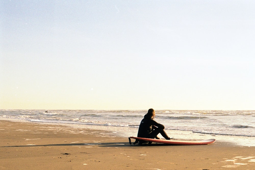 man in black shirt and pants sitting on brown surfboard on beach during daytime
