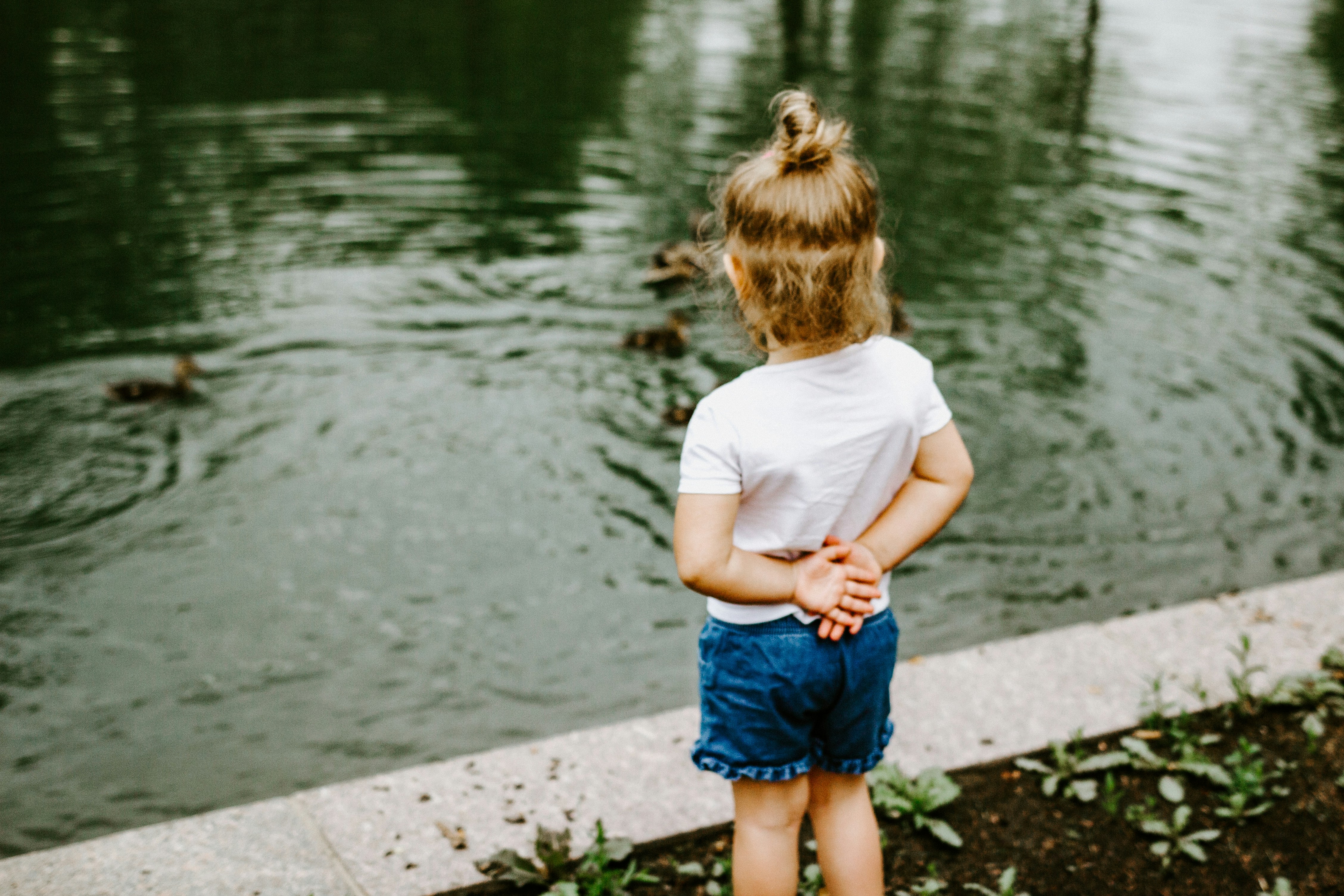 girl in white t-shirt and blue denim shorts standing on concrete pathway near body of near near near near