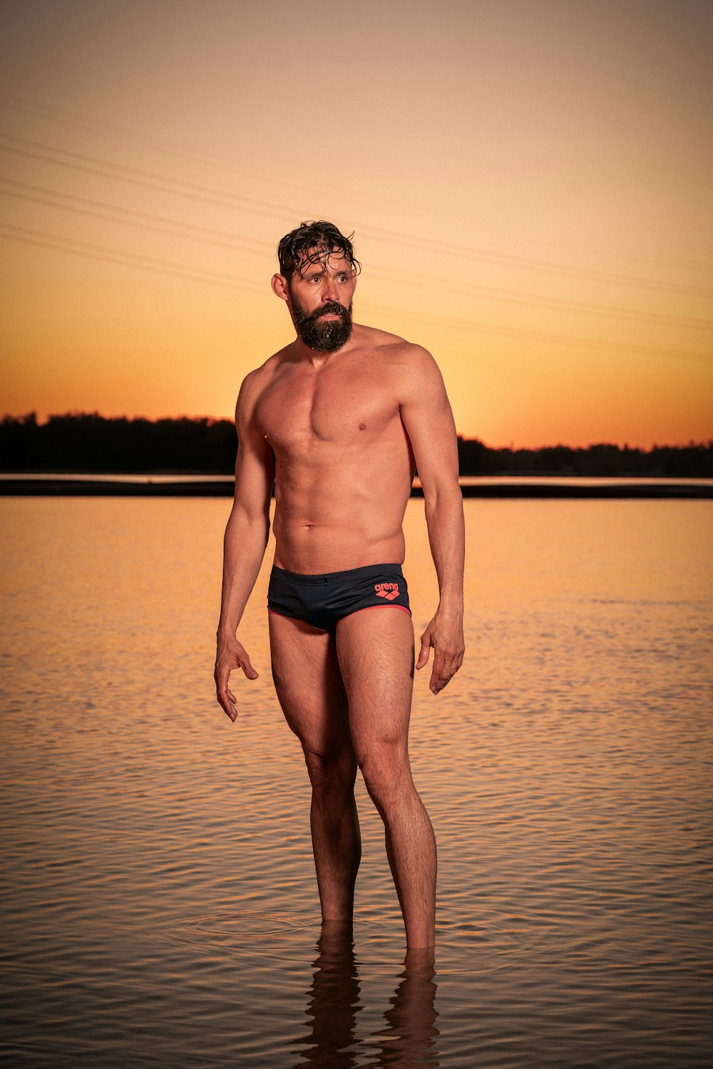 man in blue brief standing on water during sunset