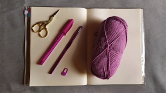 A serene workspace with pastel pink yarn, crochet hooks, and a softly lit notebook open to a crochet pattern.