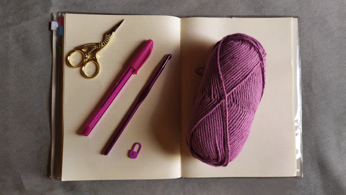 A cozy workspace with colorful crochet hooks and yarn balls scattered around a handmade notebook.