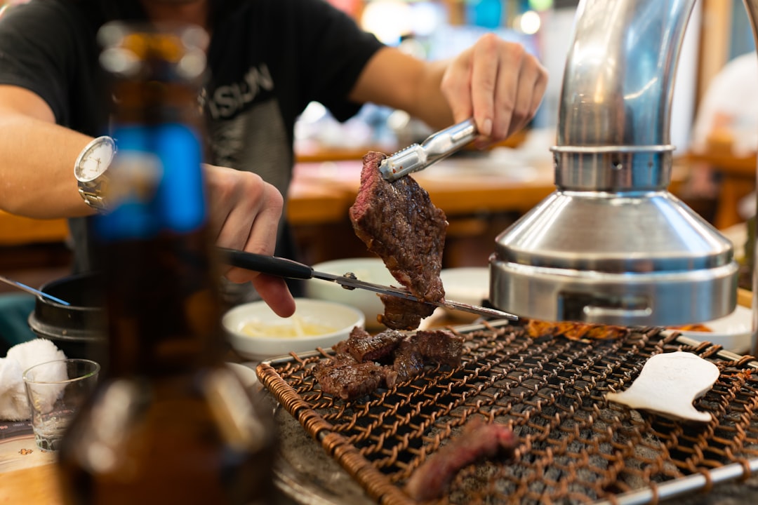 person holding stainless steel kettle, Cutting some delicious beef at a Korean BBQ restaurant.