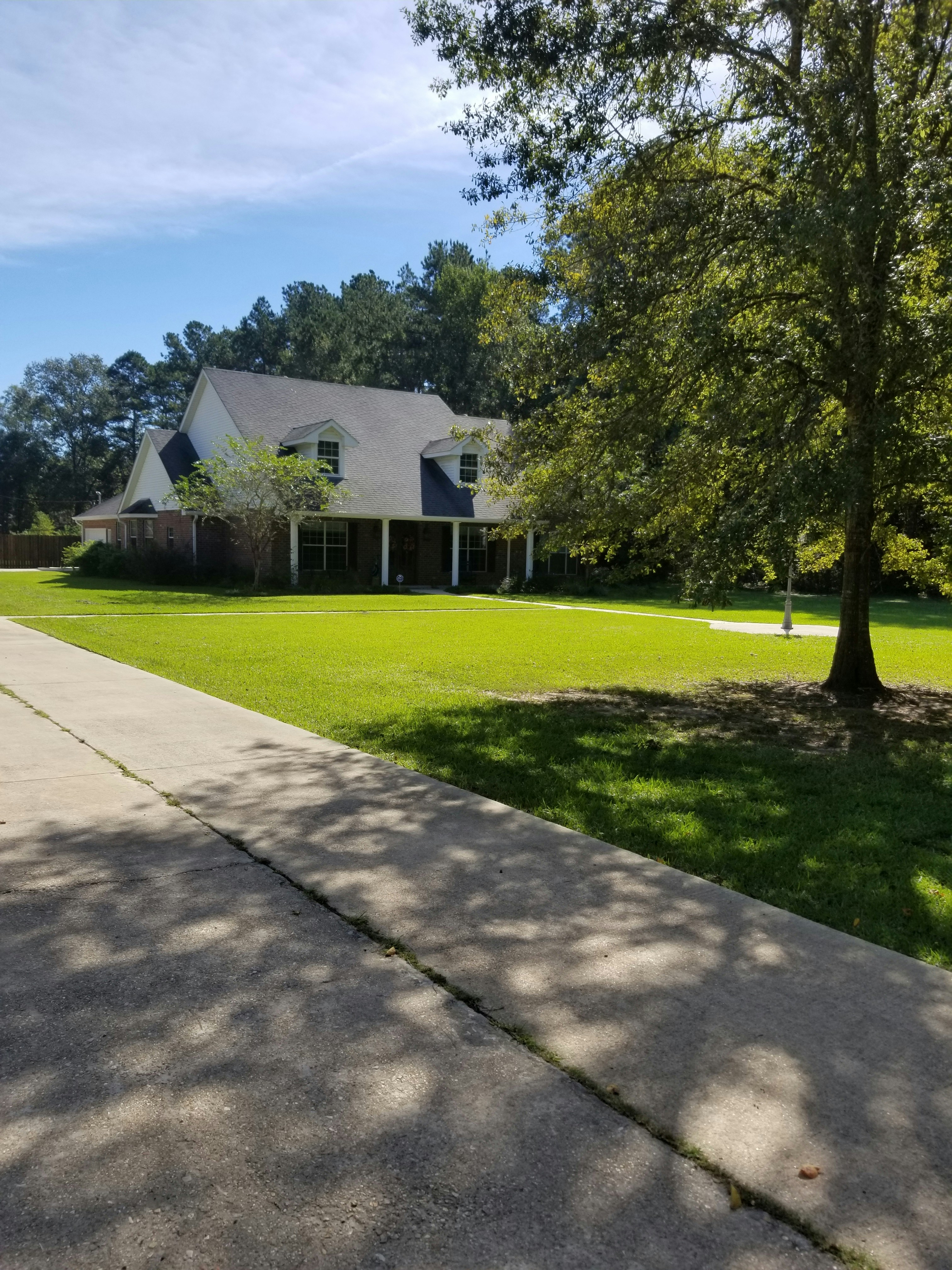 Texas suburban home with wide driveway and clear blue sky, warm midday sunlight, manicured lawn