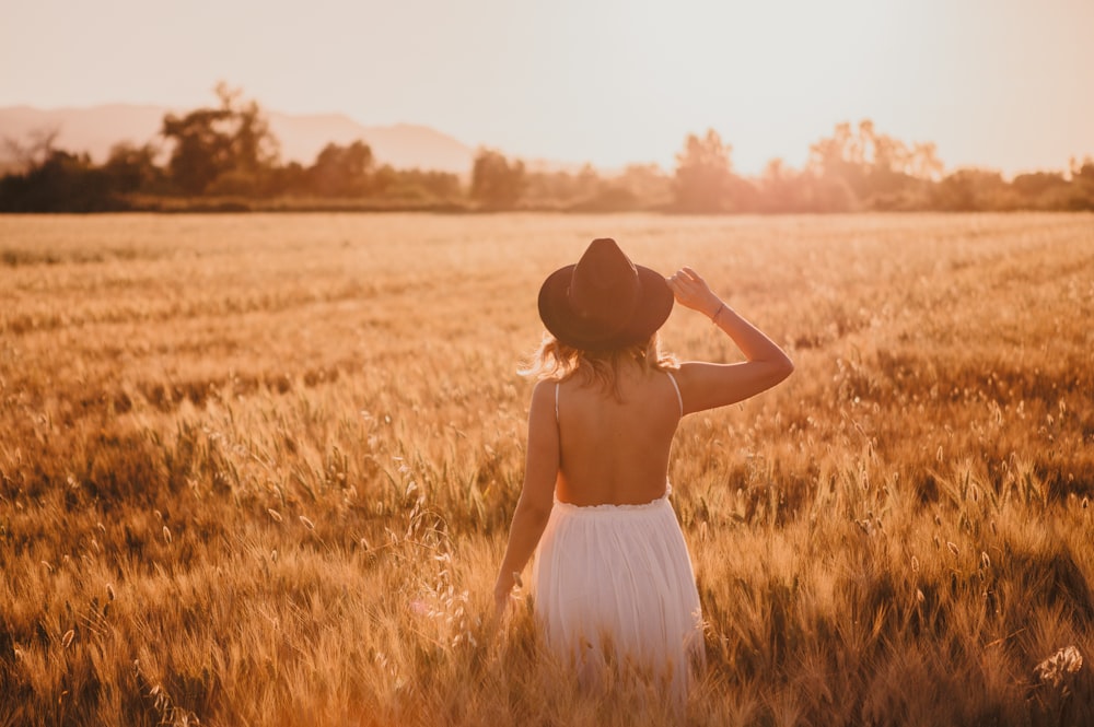 woman in white dress wearing brown hat standing on brown grass field during daytime
