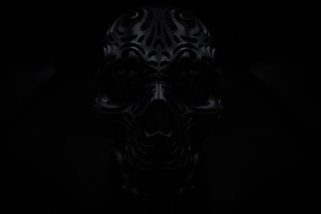 A dark image of an intricately designed, ornate skull with carved patterns. The lighting is low, adding to the mysterious and eerie atmosphere.