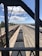 A high-angle view of a railway yard with several train tracks running parallel to each other. There is a train loaded with coal in the center track and other empty trains on adjacent tracks. The scene is framed by the structure of a bridge or an overpass, creating a rectangular border around the main view. The sky is clear with a few clouds visible, and there are trees and structures along the railway lines in the background.