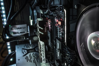 A close-up view of a computer's internal components, including a motherboard, RAM, and cooling fan. The RAM sticks have 'Trident Z Royal' branding. LED lights illuminate the area, casting a soft glow over the equipment. Various cables and connectors are neatly organized within the case.