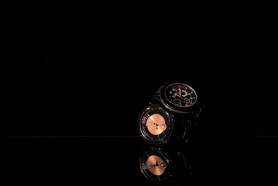An array of watches displayed on a dark surface with rim lighting emphasizing their polished edges and textures.
