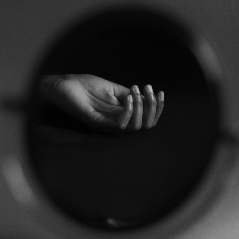 grayscale photo of persons hand on round mirror