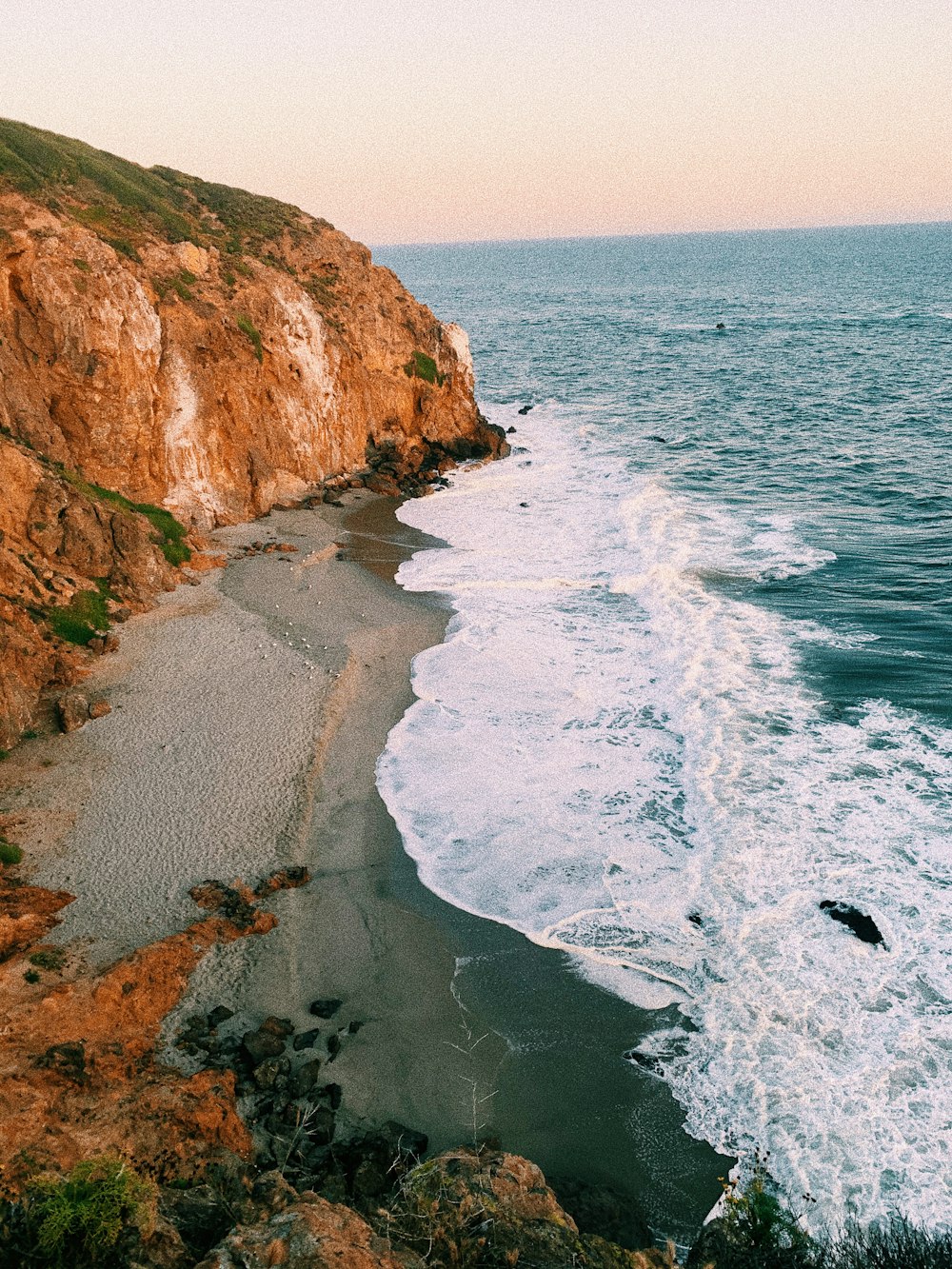 brown and green cliff beside sea during daytime