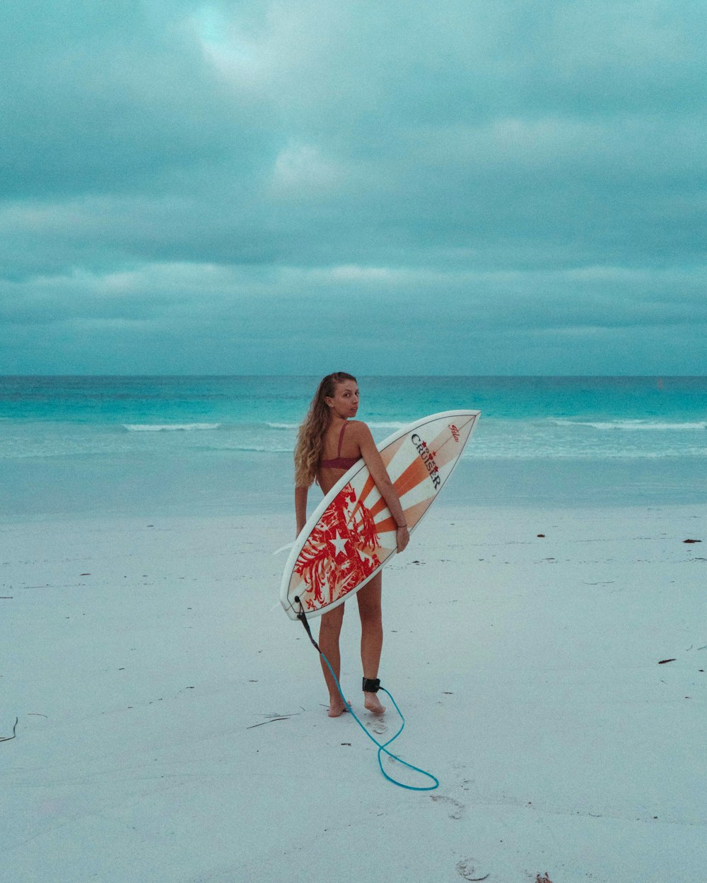woman in white and red floral dress holding white and red surfboard on beach during daytime