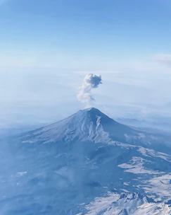 A dramatic view of Piton de la Fournaise volcano with smoke rising against a bright blue sky.