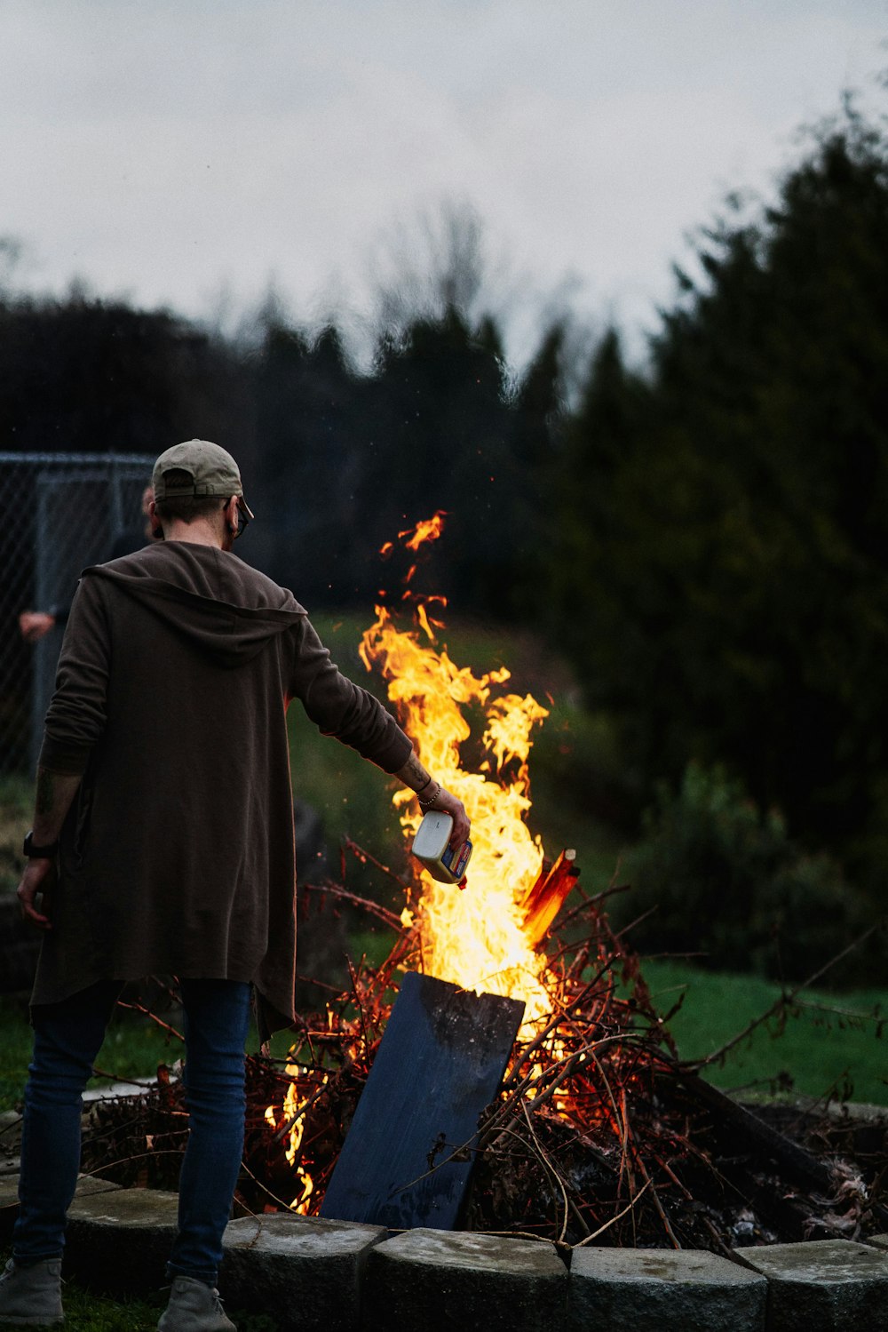 homme en sweat à capuche noir et jean bleu debout devant un feu de joie