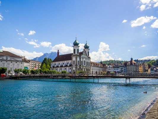 White and brown concrete building near body of water under blue sky during daytime — Lucerne, Switzerland