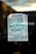 A handwritten note taped to a glass door or window, stating 'CLOSED Will Re-open in June!!' with a smiley face underneath. The sign is written with green marker on a white piece of paper and is taped at the top corners.