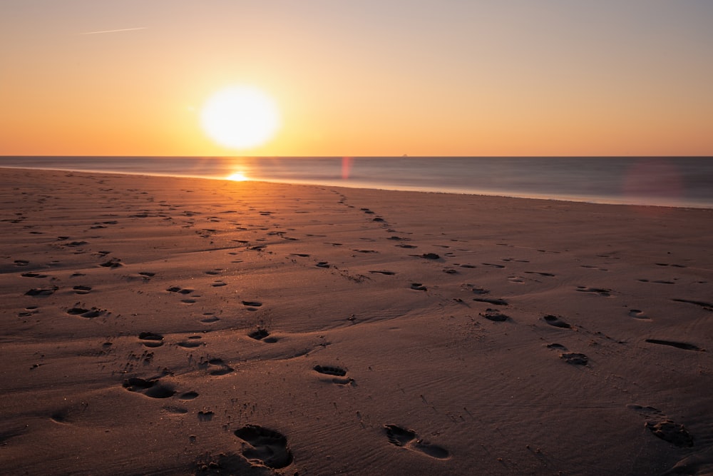 a sunset on a beach with footprints in the sand