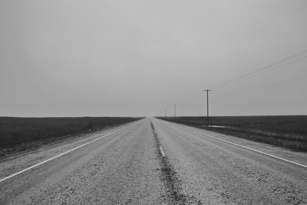 grayscale photo of road between grass field