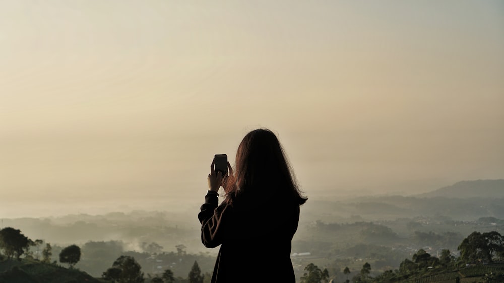 woman in black coat taking photo of mountain during daytime