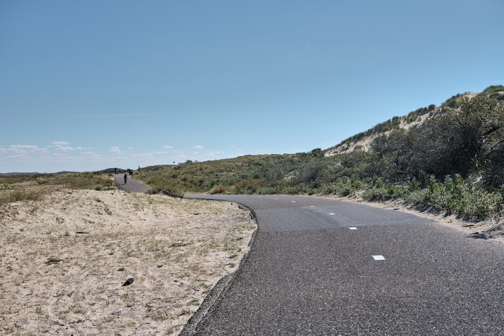 gray concrete road near green grass field under blue sky during daytime