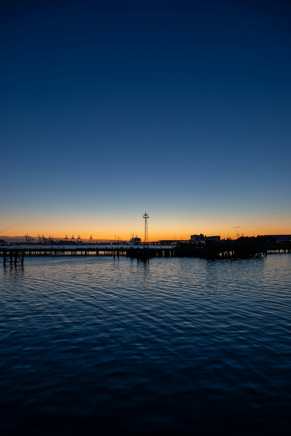 silhouette of dock on body of water during sunset